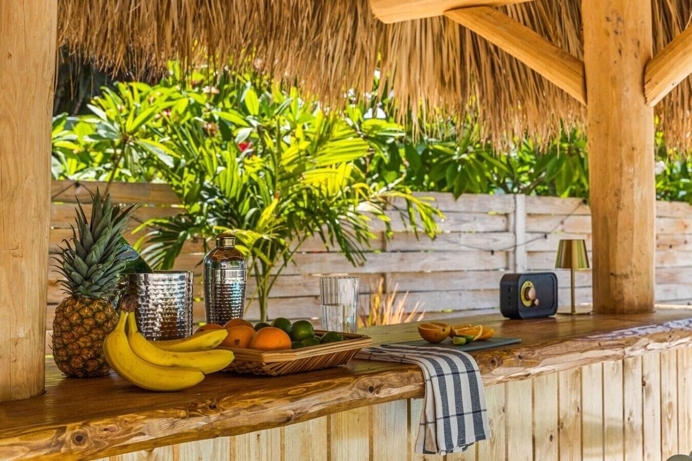 Een houten bar met rieten dak, een ananas, bananen, sinaasappels en een radio.