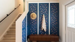 Una escalera conduce a un rellano con una pared azul decorada con un estampado de pájaros, un banco marrón y un sombrero colgado en la pared.
