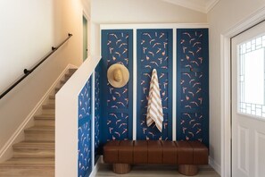 Eine Treppe führt zu einer Zwischenebene mit einer blauen Wand, die ein Vogelmuster zeigt, einer braunen Bank und einem Hut an der Wand.