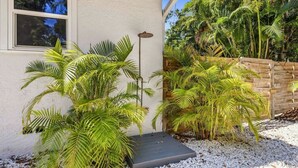 Una casa con un espacio exterior techado, palmeras y una valla de madera.