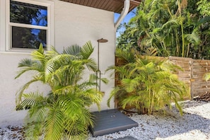 Een huis met een overdekt terras, palmbomen en een houten omheining.
