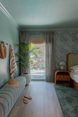 Ein Schlafzimmer mit einem Bett, einem Nachttisch, einer Topfpflanze, einer Bank und Blick ins Freie.