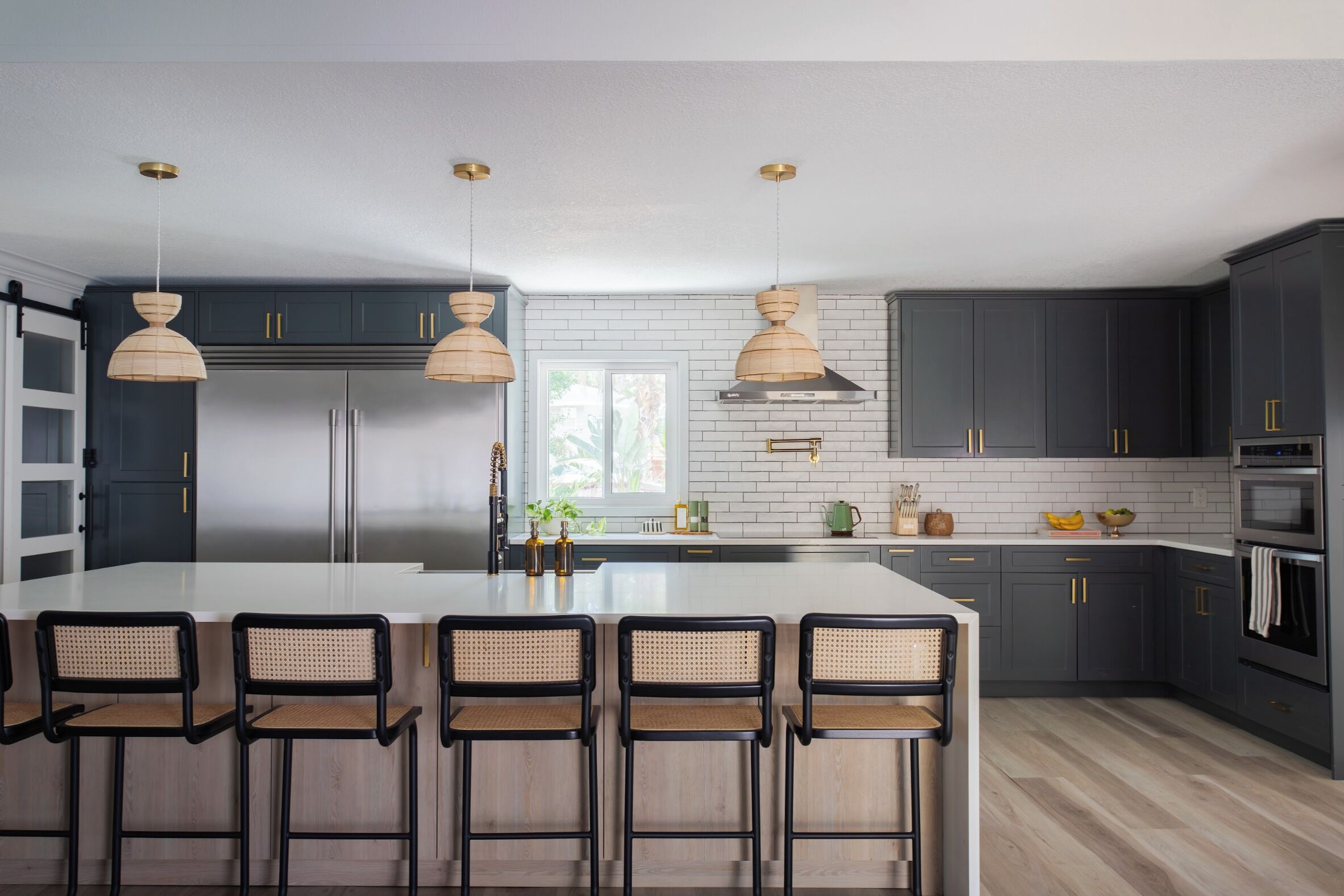 A modern kitchen with dark cabinets, a central island with bar stools, stainless steel appliances, and pendant lighting.