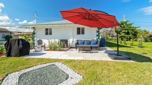 A house with a patio, a red umbrella, outdoor furniture, and a barbecue grill. - 3BR 2BA with Modern Interior & Backyard (Oakland Park)