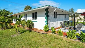 A single-story house with a green and white exterior, a fenced patio area with outdoor furniture, and a small garden with palm trees and shrubs. - 3BR 2BA with Modern Interior & Backyard (Oakland Park)