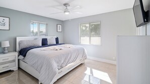 A bedroom with a bed, nightstand, wall-mounted TV, ceiling fan, and windows. - 3BR 2BA with Modern Interior & Backyard (Oakland Park)