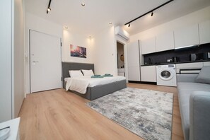 A compact bedroom with a bed, a washing machine, and a kitchenette. - New Centre Studio with Balcony (Limassol)