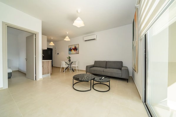 Una sala de estar moderna con un sofá gris, dos mesas auxiliares negras, una mesa de comedor con sillas e iluminación colgante.