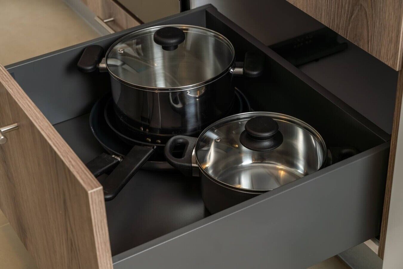 A kitchen drawer with two stainless steel pots.