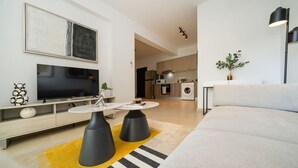 En moderne stue med et fladskærms-tv, en sofa, to sorte sofaborde og en gul tæppe.