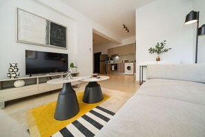 A modern living room with a flat-screen TV, a sofa, two black coffee tables, and a yellow rug.