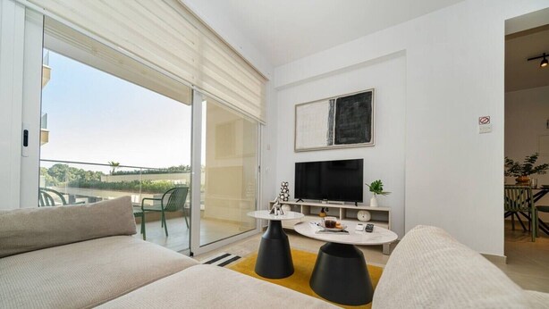 En moderne stue med sofa, sofabord, fjernsyn og en skydedør til et udendørs område.