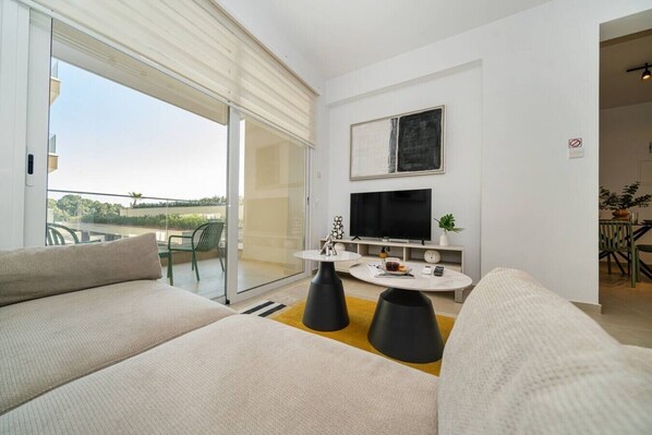 A modern living room with a sofa, a coffee table, a TV, and a sliding glass door leading to an outdoor area.