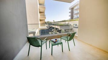 Ein Balkon mit zwei grünen Stühlen, einem kleinen Tisch und freiem Blick auf angrenzende Gebäude und einen Parkplatz.