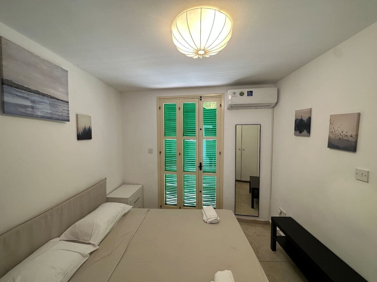 Un dormitorio con cama, mesita de noche y armario con contraventanas verdes.