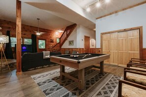 Ein Billardtisch in einem Raum mit Holzwänden, einer Treppe und einer großen Holztür.