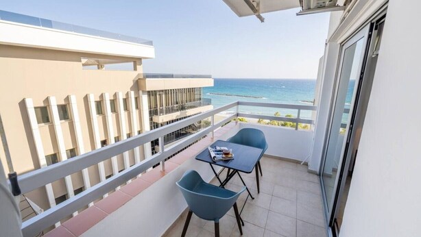 Ein Balkon mit Tisch und Stühlen, Blick aufs Meer und ein Gebäude im Hintergrund.