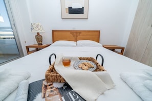 A hotel room with a bed, a bedside table with a lamp, a framed picture on the wall, and a tray with a drink and snacks on the bed.