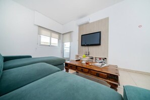 A modern living room with a sofa, a wooden coffee table, and a flat-screen TV mounted on the wall.