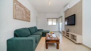 Ein modernes Wohnzimmer mit einer Eckcouch, einem Holztisch und einem Flachbildfernseher an einer Wand aus Holzpaneelen.