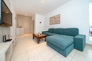 A modern living room with a sectional sofa, a wooden coffee table, and a flat-screen TV mounted on the wall.