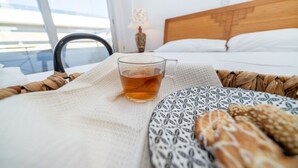 Ein Hotelzimmer mit Bett, Nachttisch mit Lampe, einer Teetasse und einem Korb mit Brot.