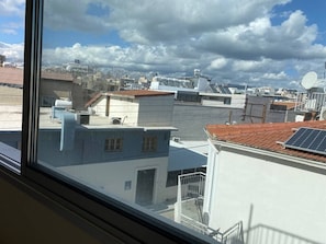Vista de edificios con techos planos y antenas parabólicas, a través de una ventana con marco de metal.