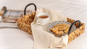 Ein geflochtener Korb mit einer Speisenplatte und einer Tasse Tee auf einem Bett.
