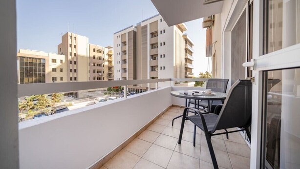 Ein Balkon mit Tisch und Stühlen, Blick auf umliegende Gebäude und einen klaren Himmel.