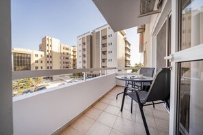 Ein Balkon mit Tisch und Stühlen, Blick auf umliegende Gebäude und einen klaren Himmel.