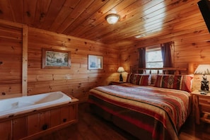 Ein Zimmer in einer Holzh ütte mit einem Bett, einem kleinen Tisch, einem Nachttisch, einem Fenster und einem an der Wand hängenden Bild.