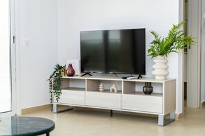 Un saló modern amb un televisor de pantalla plana sobre un moble blanc, una planta en test i una taula petita.