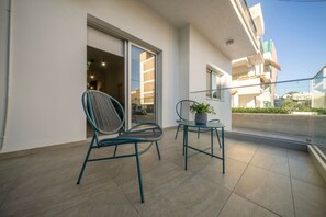 Ein Balkon mit zwei Stühlen, einer davon mit einer Pflanze, und einer Schiebetür zu einem Innenraum.