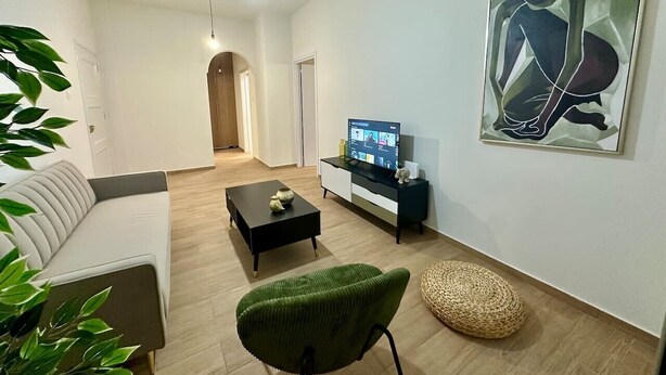 Un saló modern amb un sofà, una cadira verda, una taula de centre, una televisió sobre un moble i un quadre a la paret.
