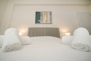 Ein Hotelzimmer mit einem Bett, zwei Nachttischlampen, einem Bild an der Wand und zwei aufgerollten Handtüchern.