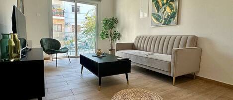 Una sala de estar con sofá, mesa de centro, reposapiés, mueble para televisión y una planta.