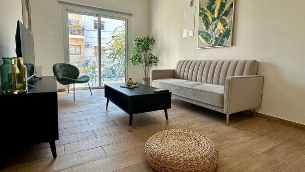 Una sala de estar con sofá, mesa de centro, reposapiés, mueble para televisión y una planta.