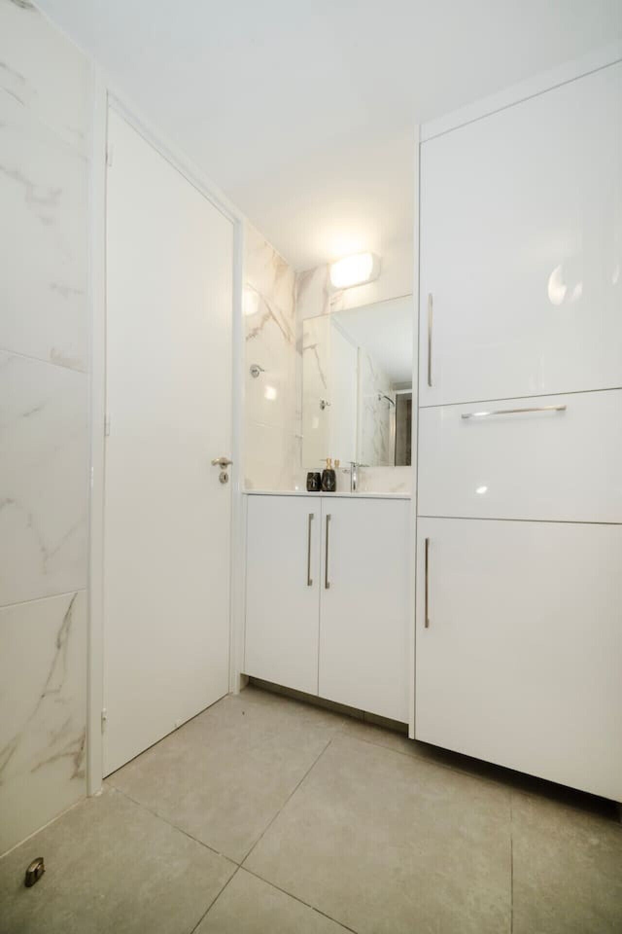 A bathroom with a white door, a mirror, and cabinets.