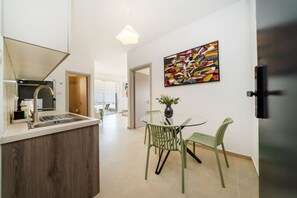 A modern kitchen with a central island, a dining area with a glass table and chairs, and a colorful abstract painting on the wall.