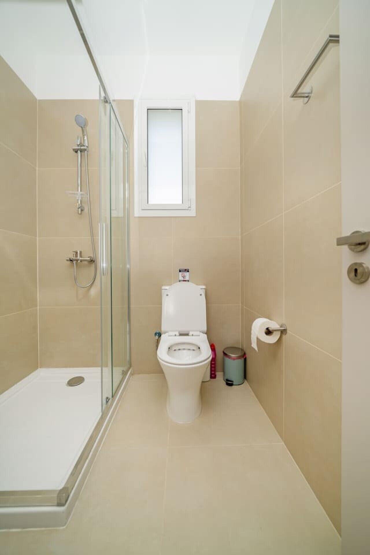 Une salle de bain avec une douche à parois de verre, des toilettes et une petite fenêtre.