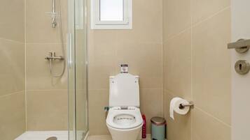 Une salle de bain avec une douche à parois de verre, des toilettes et une petite fenêtre.