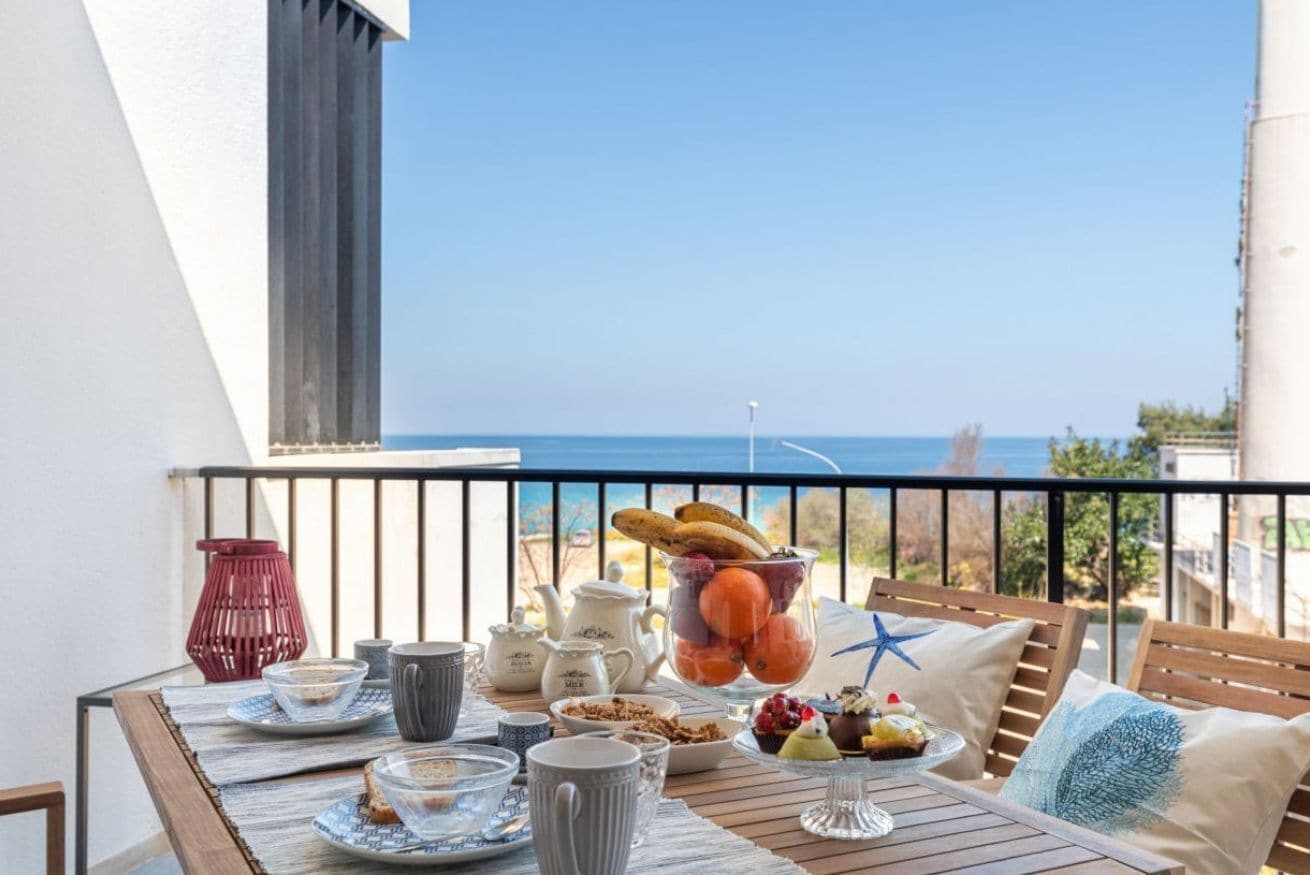 A balcony with a table set for breakfast, overlooking a clear blue sea.