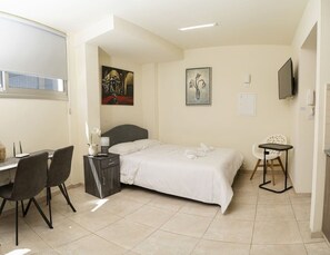 A bedroom with a bed, a desk, a chair, a small table, and artwork on the walls. - Modern stylish studio, historic center, near beach (Limassol)