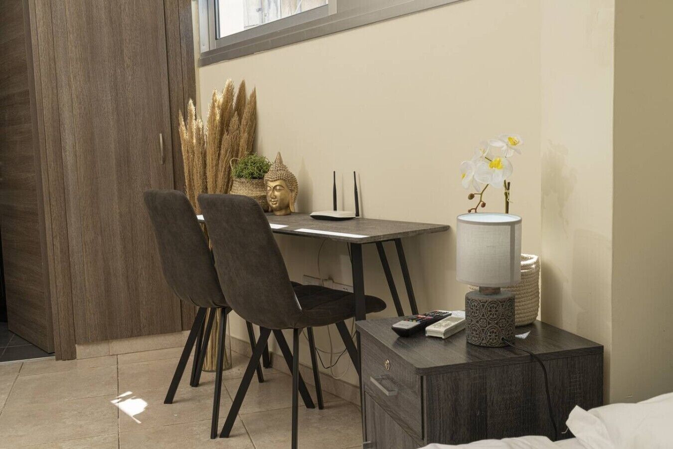 Een kleine, moderne kamer met een bureau, twee stoelen, een lamp en een Boeddhabeeld.