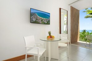 A modern room with a glass table, white chairs, a fruit bowl, and a large window with a view of a beach and ocean. - Beachfront Luxury Studio • Ultravioleta Cabarete (Cabarete)