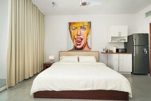A hotel room with a large bed, a painting on the wall, a kitchen area with cabinets, and a refrigerator. - Beachfront Luxury Studio • Ultravioleta Cabarete (Cabarete)