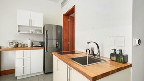 Eine moderne Küche mit weißen Schränken, einem Edelstahlkühlschrank, einer Holz Arbeitsplatte, einer Spüle und einer Kaffeemaschine.
