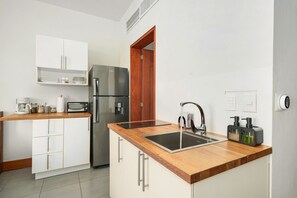 A modern kitchen with white cabinetry, a stainless steel refrigerator, a wooden countertop, a sink, and a coffee maker. - Beachfront Luxury Studio • Ultravioleta Cabarete (Cabarete)