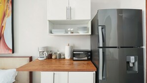 Eine Küchenzeile mit Edelstahlkühlschrank, einer Kaffeemaschine, einem Toaster und einem Regal mit Tellern und Schüsseln.