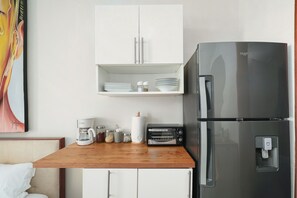 A kitchenette with a stainless steel refrigerator, a coffee maker, a toaster, and a shelf with plates and bowls. - Beachfront Luxury Studio • Ultravioleta Cabarete (Cabarete)